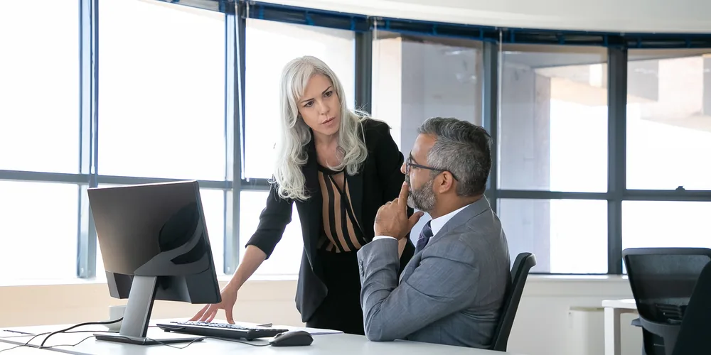 Bras droit des dirigeants : échange de travail entre une collaboratrice et un chef d'entreprise devant un écran