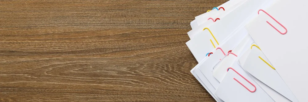 Courriers et documents classés avec des trombones sur un bureau en bois